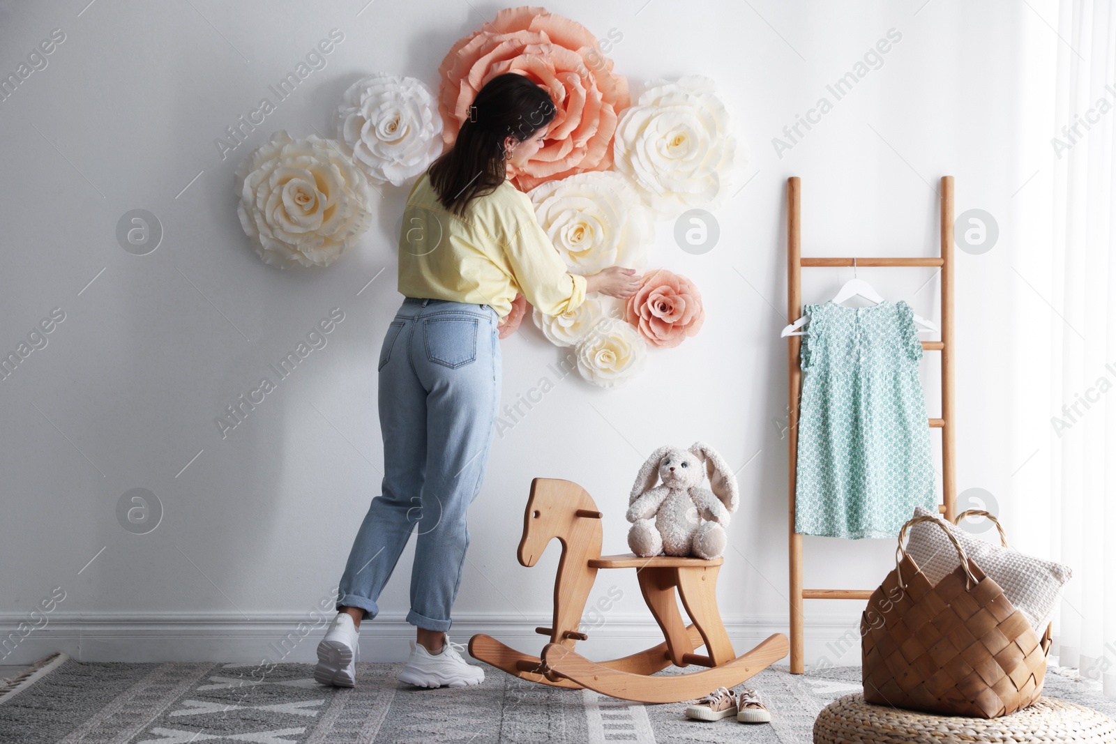 Photo of Woman decorating wall with beautiful paper flowers in child's room