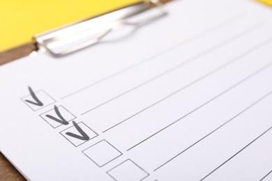 Photo of Checklist with marked checkboxes on yellow background, closeup