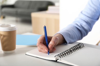 Photo of Woman taking notes at white table indoors, closeup. Self-study