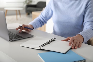 Photo of Woman learning online using laptop and taking notes at white table indoors, closeup. Self-study