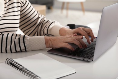 Photo of Woman learning online using laptop at white table indoors, closeup. Self-study