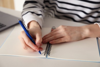 Photo of Woman taking notes at white table indoors, closeup. Self-study