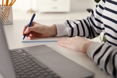 Photo of Woman taking notes during online lesson at white table indoors, closeup. Self-study