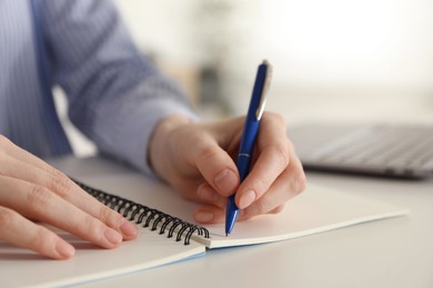 Photo of Woman taking notes at white table indoors, closeup. Self-study