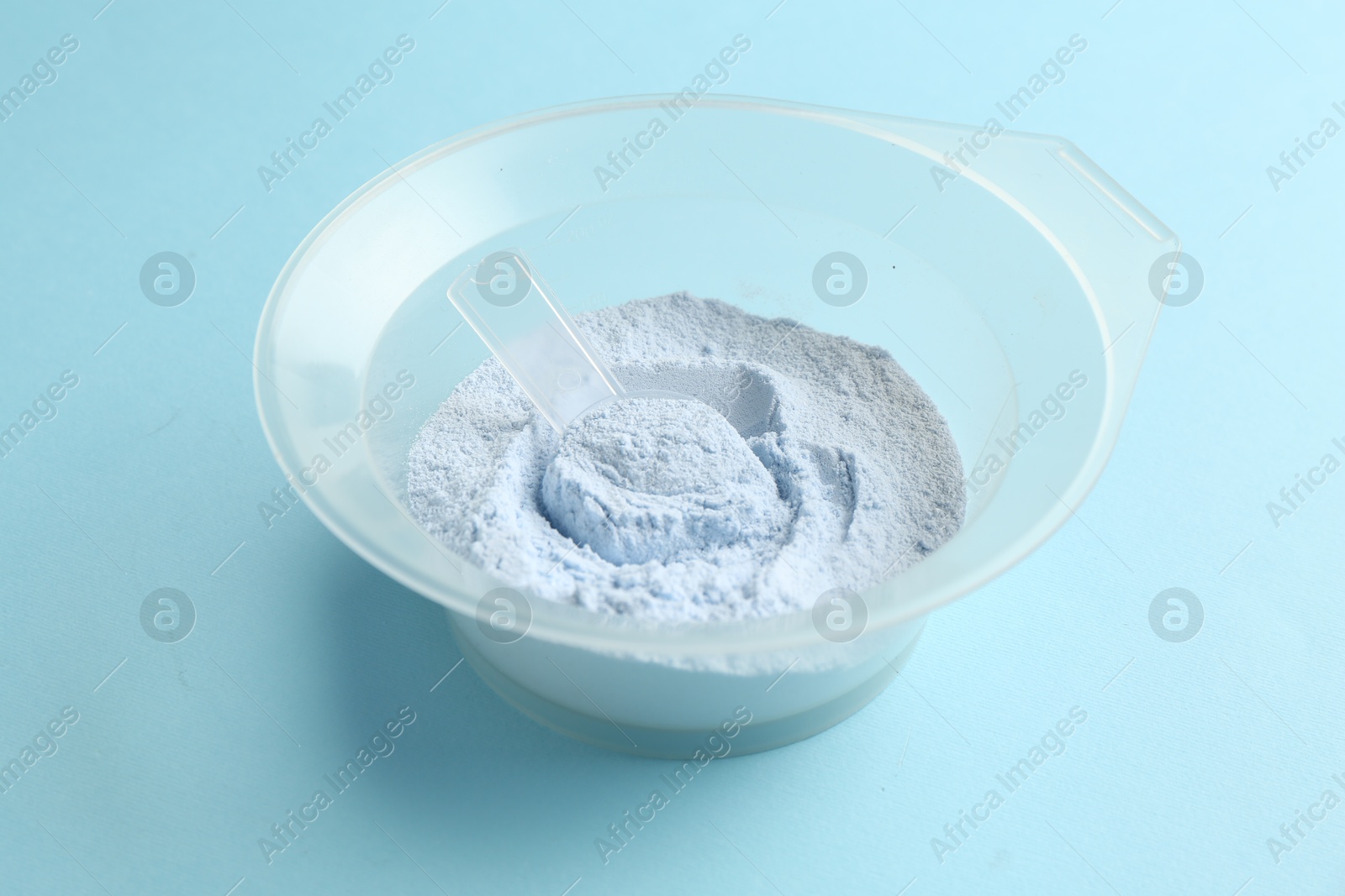 Bowl with hair bleaching powder on light blue background, closeup Photo of Bowl with hair bleaching powder on light blue background, closeup