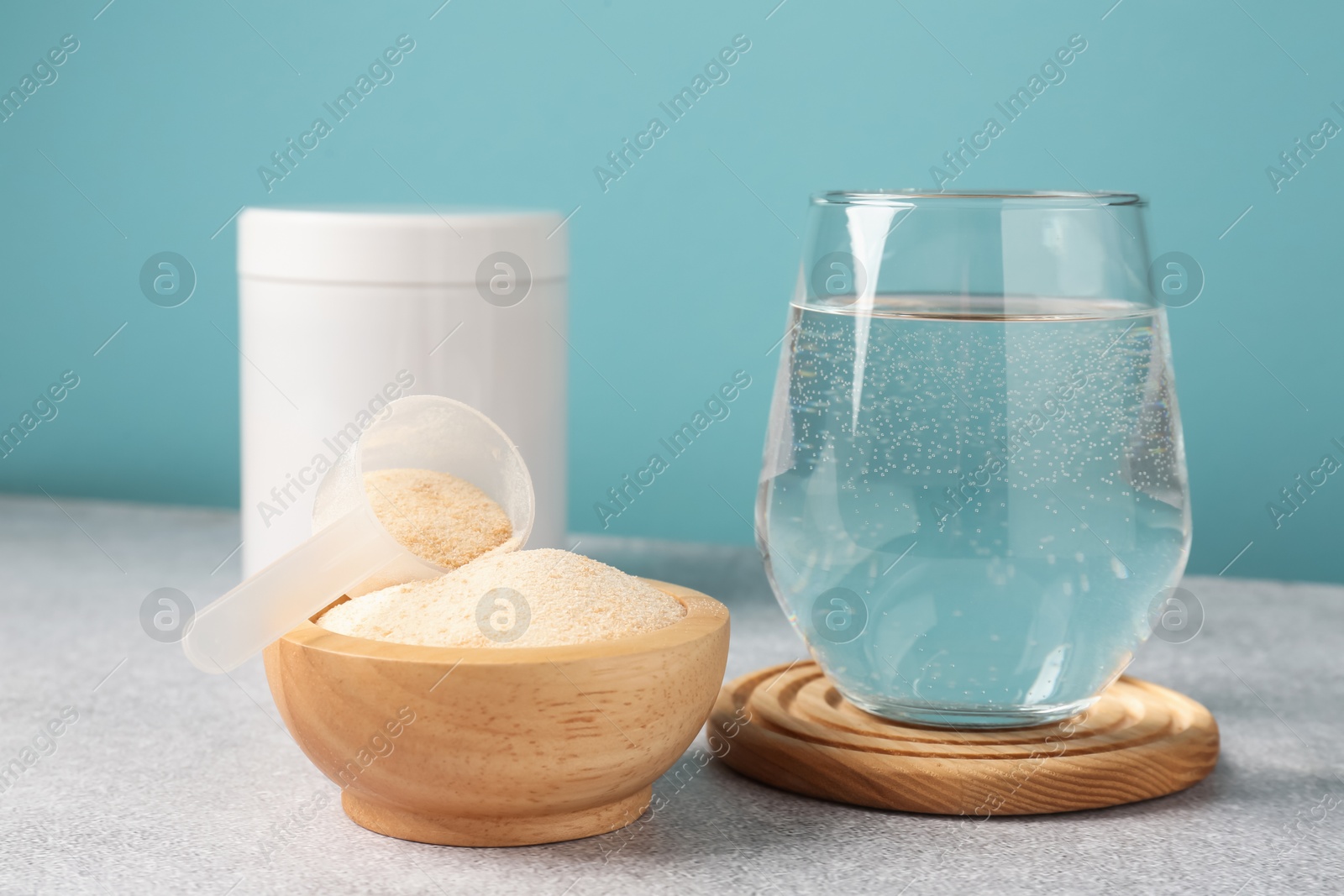 Collagen powder and glass of water on grey textured table against light blue background, closeup Photo of Collagen powder and glass of water on grey textured table against light blue background, closeup