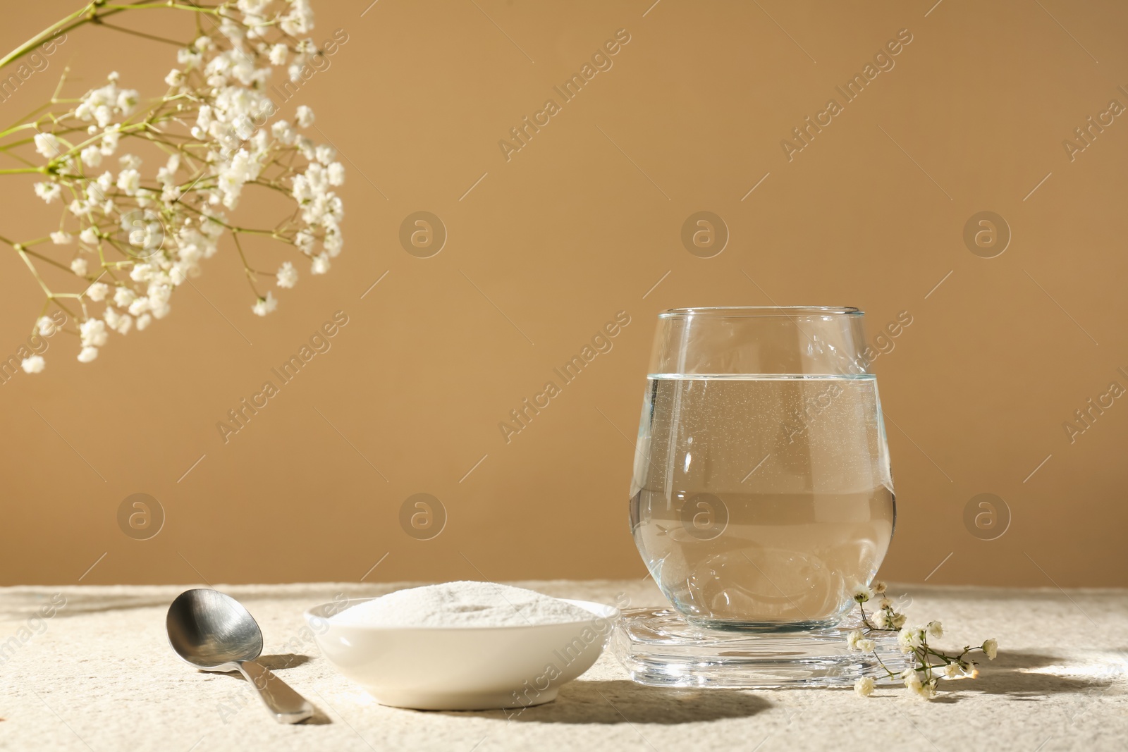 Collagen powder in bowl, spoon, glass of water and gypsophila branches on light textured table against beige background, closeup Photo of Collagen powder in bowl, spoon, glass of water and gypsophila branches on light textured table against beige background, closeup