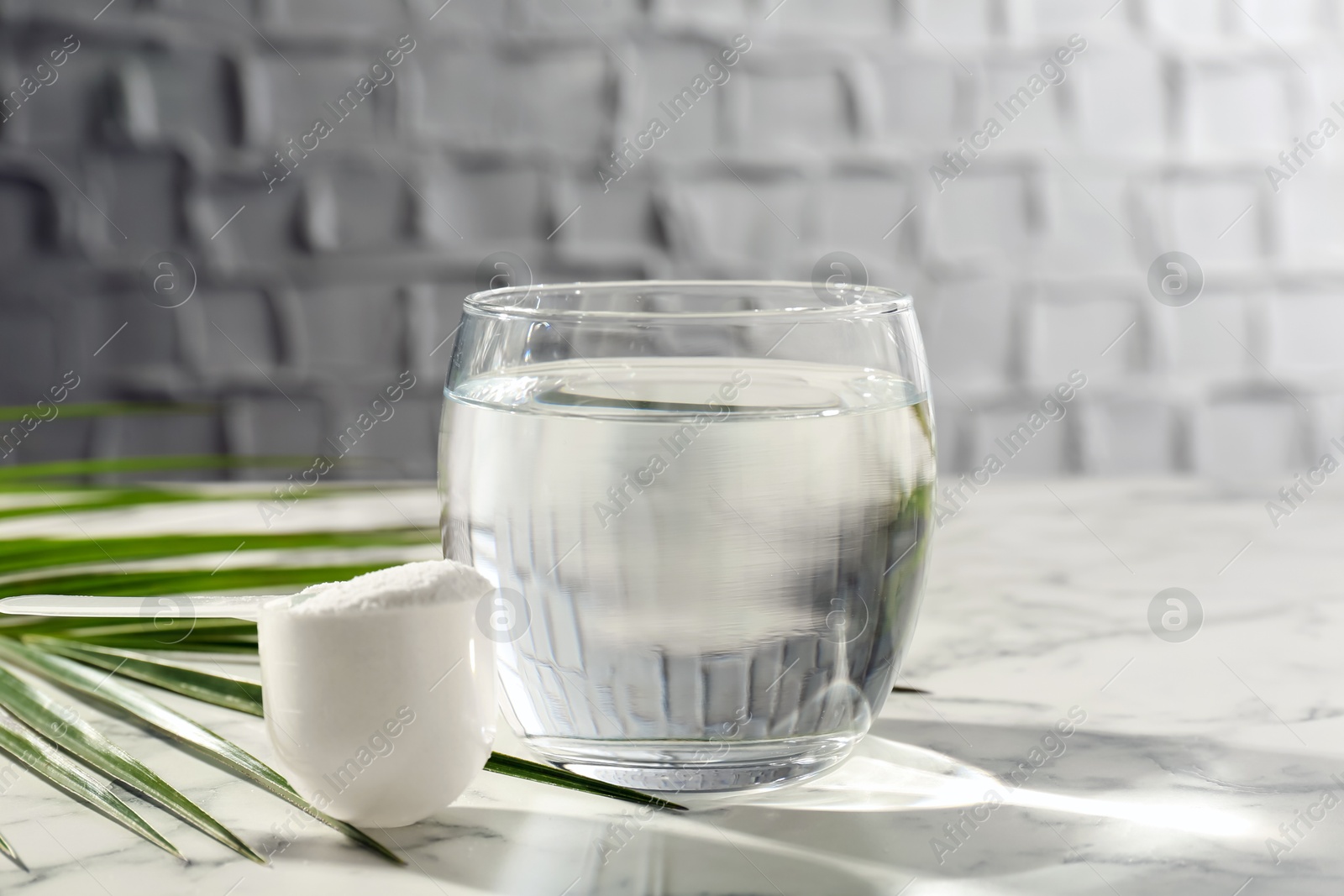 Collagen powder in scoop, glass of water and palm leaf on light marble table Photo of Collagen powder in scoop, glass of water and palm leaf on light marble table