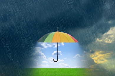 Image of Open colorful umbrella revealing green meadow under blue sky during heavy rainstorm