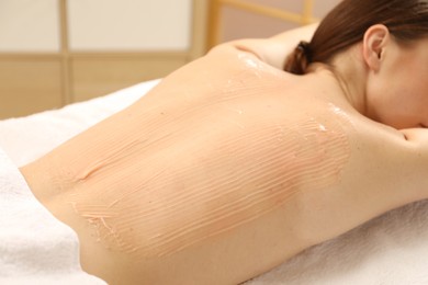 Photo of Woman undergoing body wraps treatment in spa salon, closeup