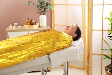 Photo of Woman covered with thermal foil blanket undergoing body wraps treatment in spa salon