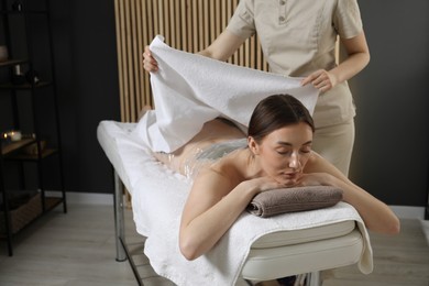 Photo of Spa body wraps. Esthetician covering woman with sheet indoors, closeup