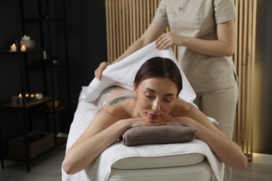 Photo of Spa body wraps. Esthetician covering woman with sheet indoors, closeup