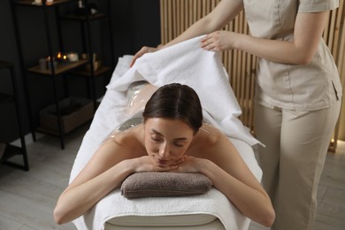 Photo of Spa body wraps. Esthetician covering woman with sheet indoors, closeup