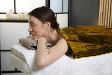 Photo of Woman covered with thermal foil blanket undergoing body wraps treatment in spa salon