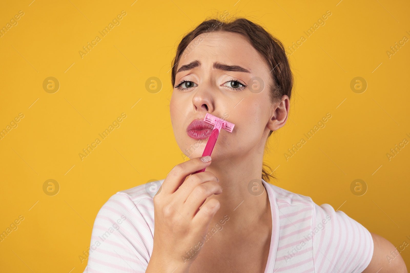 Photo of Beautiful woman shaving her mustache with razor on light green background