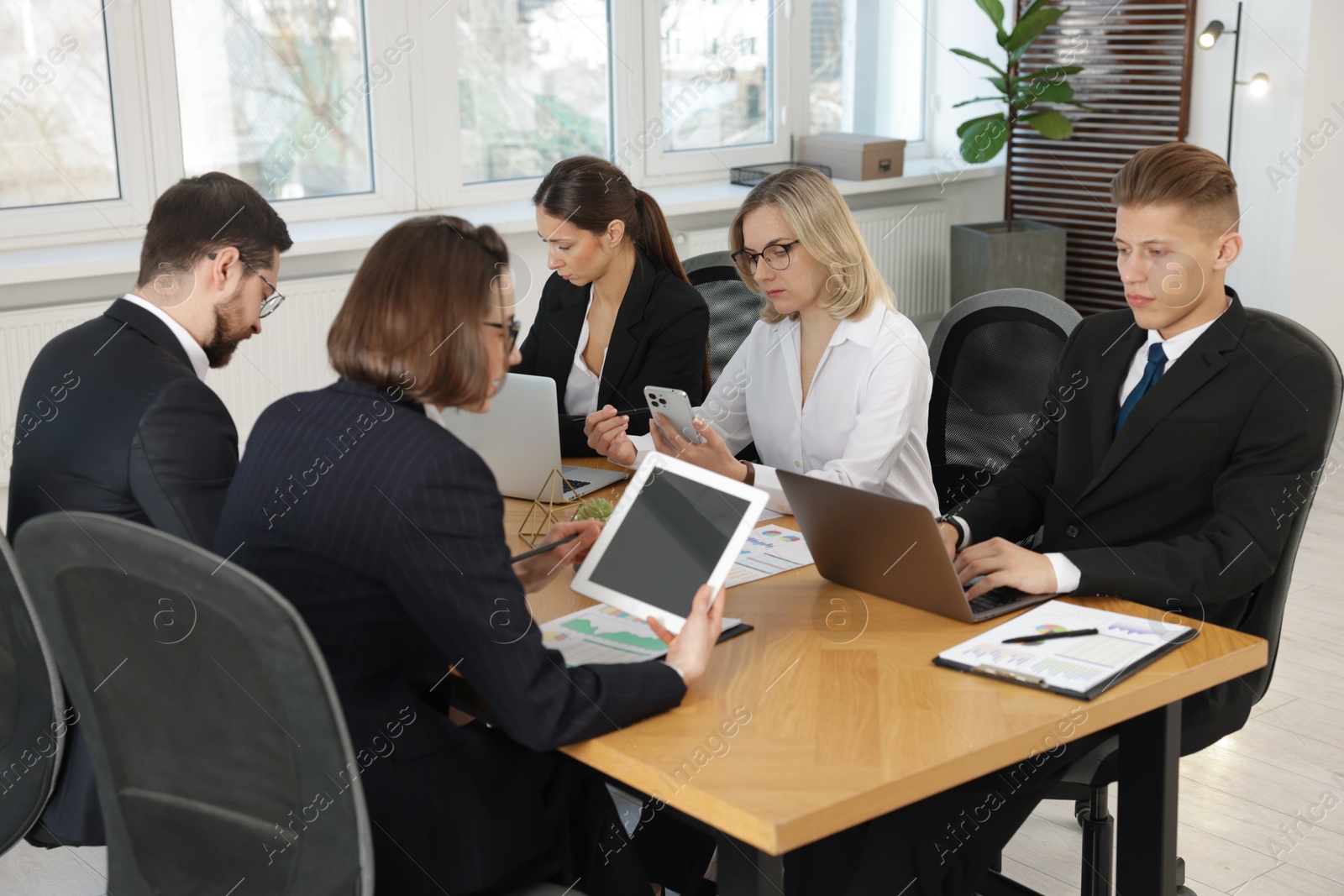 Photo of Coworkers with different devices working together at wooden table in office