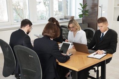 Photo of Coworkers with different devices working together at wooden table in office