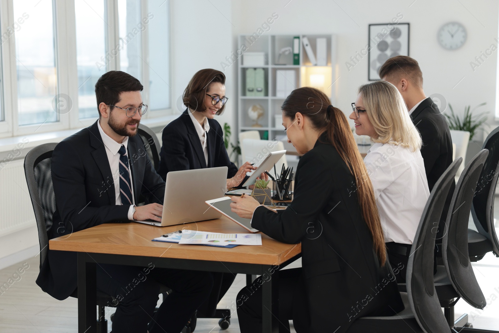 Photo of Coworkers with different devices working together at wooden table in office