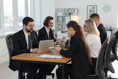 Photo of Coworkers with different devices working together at wooden table in office