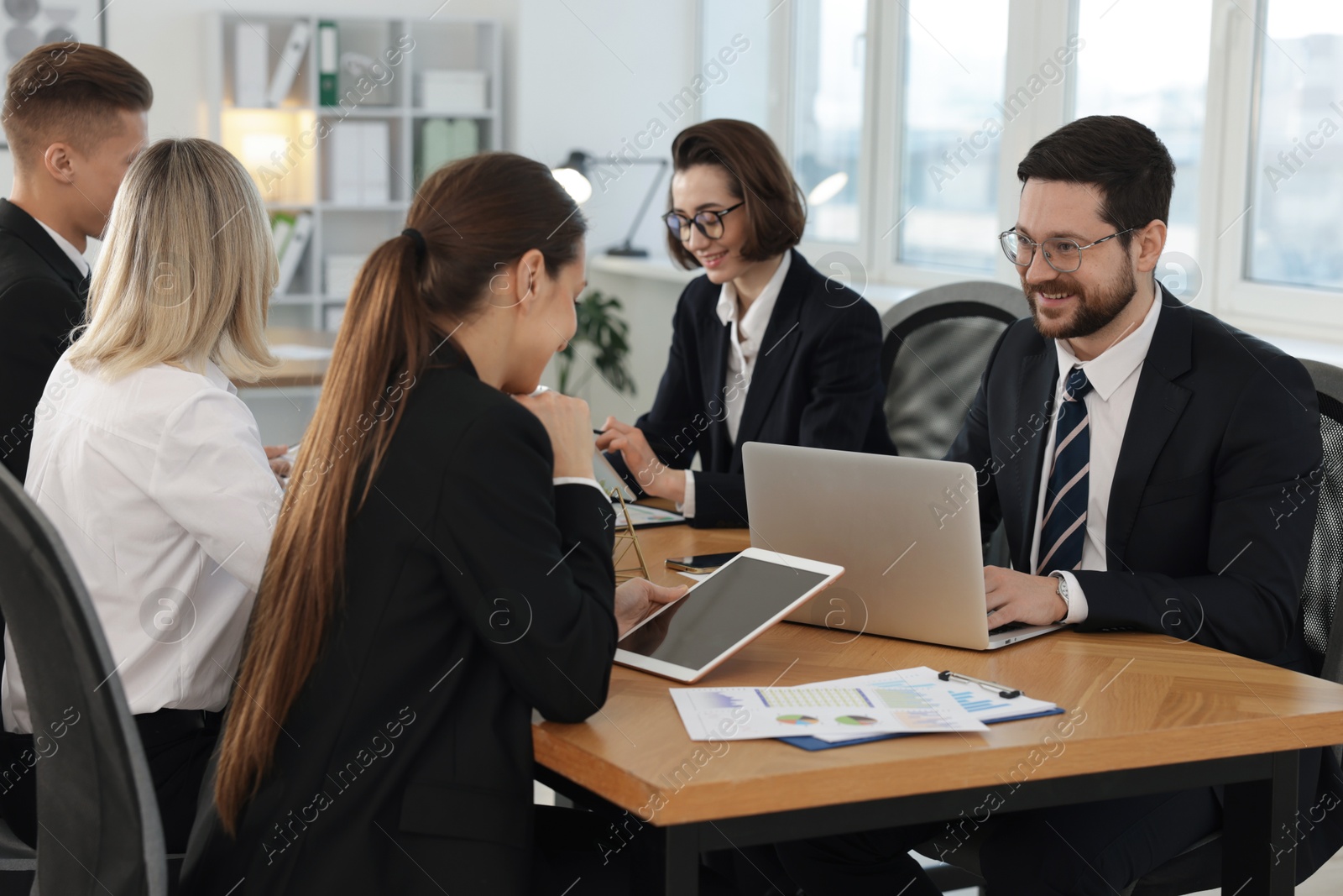 Photo of Coworkers with different devices working together at wooden table in office