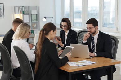 Photo of Coworkers with different devices working together at wooden table in office