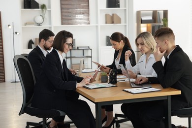 Photo of Coworkers with different devices working together at wooden table in office