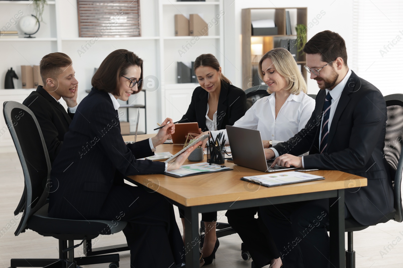 Photo of Coworkers with different devices working together at wooden table in office