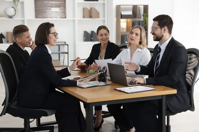 Photo of Coworkers working together at wooden table in office