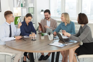 Photo of Coworkers working together at wooden table in office