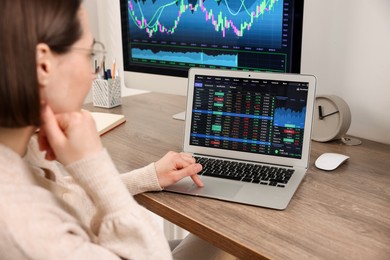 Photo of Stock exchange. Woman analysing financial market on laptop at wooden table indoors