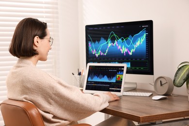 Photo of Stock exchange. Woman analysing financial market on laptop at wooden table indoors