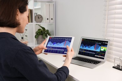 Photo of Stock exchange. Woman analysing financial market on tablet at white table indoors