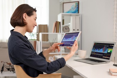 Photo of Stock exchange. Woman analysing financial market on tablet at white table indoors