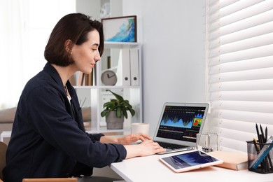 Photo of Stock exchange. Woman analysing financial market on laptop at white table indoors