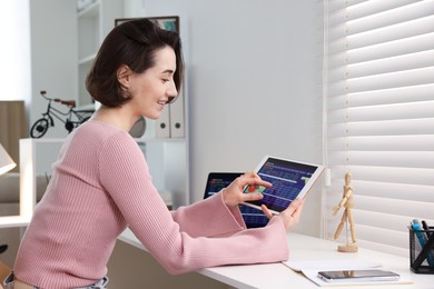 Photo of Stock exchange. Woman analysing financial market on tablet at white table indoors