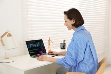 Photo of Stock exchange. Woman analysing financial market on laptop at white table indoors