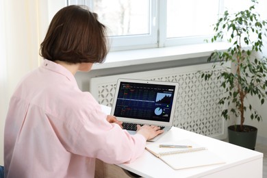 Photo of Stock exchange. Woman analysing financial market on laptop at white table indoors