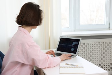 Photo of Stock exchange. Woman analysing financial market on laptop at white table indoors