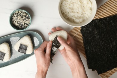 Photo of Woman making tasty onigiri (Japanese rice balls) at white table, top view