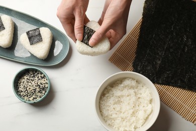 Photo of Woman making tasty onigiri (Japanese rice balls) at white table, top view