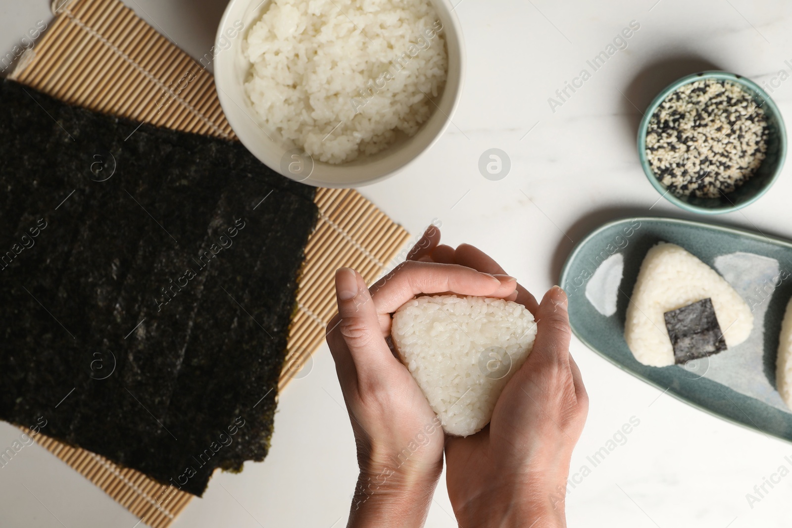 Woman making tasty onigiri (Japanese rice balls) at white table, top view Photo of Woman making tasty onigiri (Japanese rice balls) at white table, top view