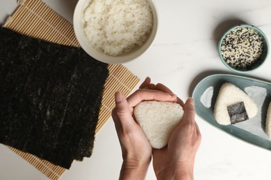 Photo of Woman making tasty onigiri (Japanese rice balls) at white table, top view