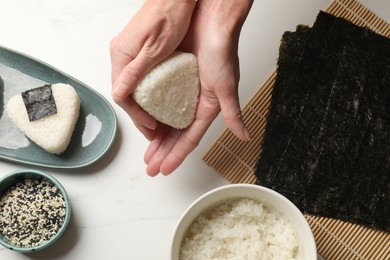 Photo of Woman making tasty onigiri (Japanese rice balls) at white table, top view