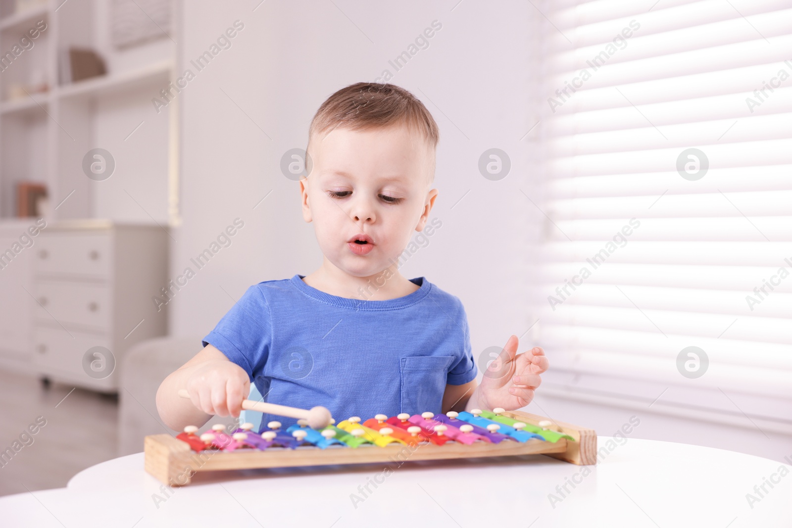 Photo of Motor skills development. Little boy playing with xylophone at white table indoors