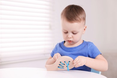 Photo of Motor skills development. Little boy playing with lacing toy at white table indoors, space for text