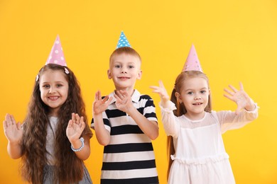 Photo of Children in conical paper hats on yellow background. Birthday surprise party