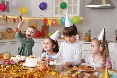 Photo of Children at table with tasty cake and different treats indoors. Birthday surprise party