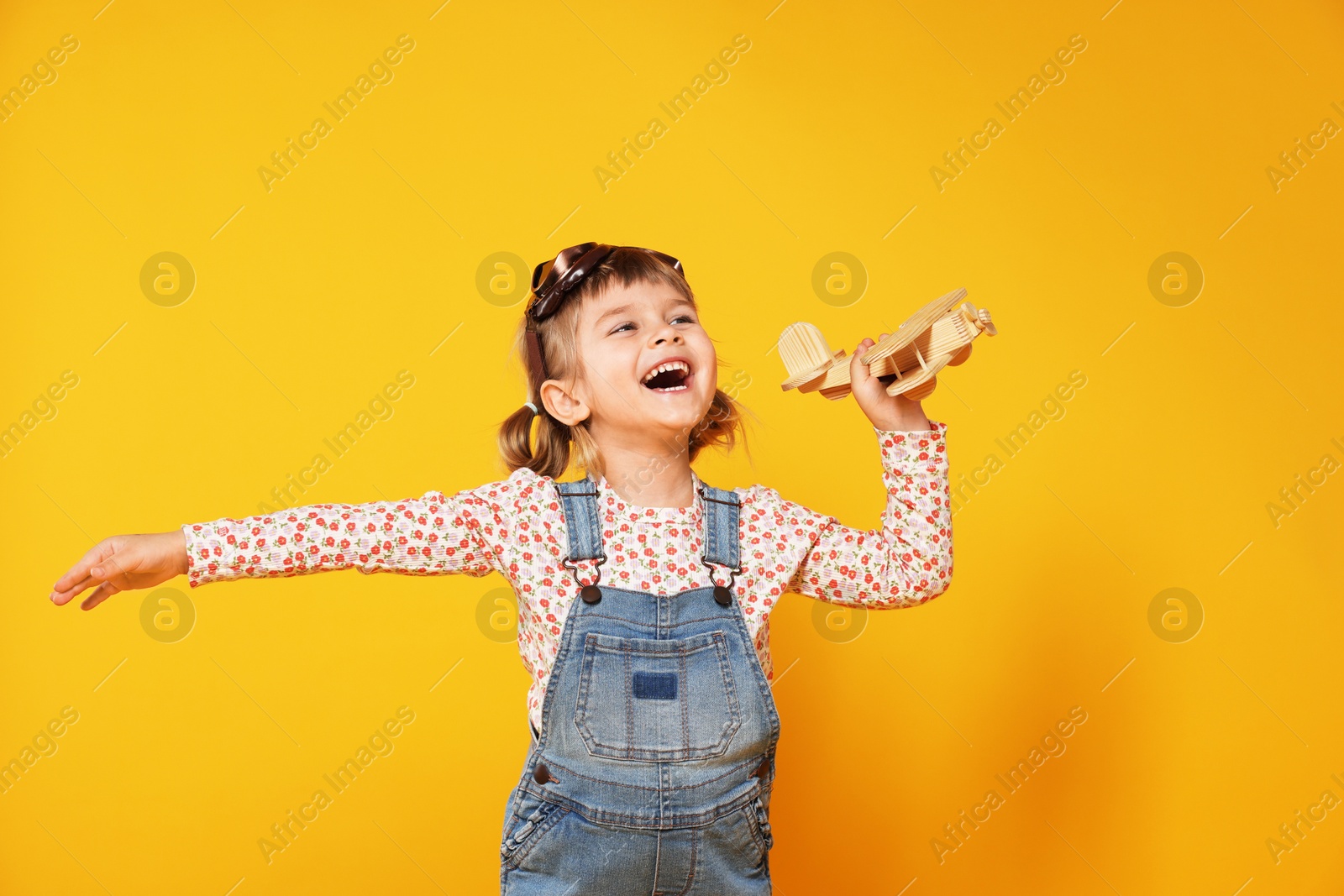 Photo of Happy little girl playing with toy plane on orange background