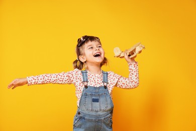 Photo of Happy little girl playing with toy plane on orange background